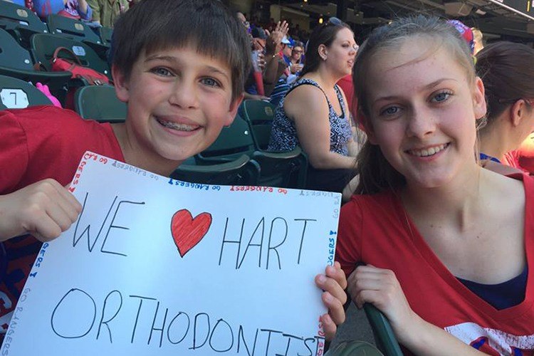 Kids at baseball game holding a we love hart orthodontics sign